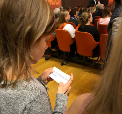 En flicka med grå tröja och mörkblont hår läser en lapp